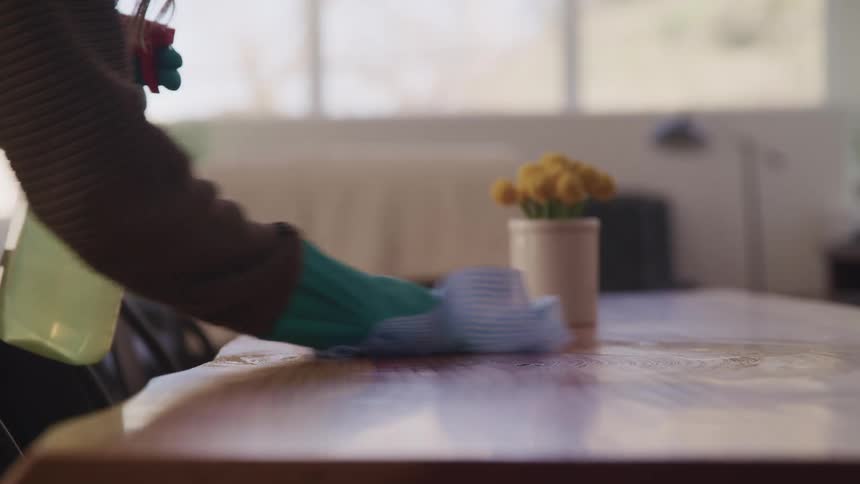A person is cleaning a table with a rag and spray bottle