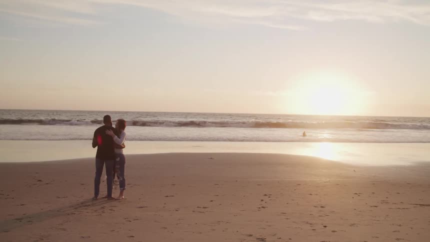 A man and woman embrace closely standing on the sandy beach