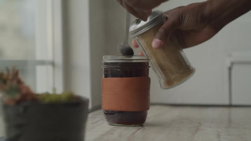 Black person shakes a spice into a beverage glass then stirs it with a spoon