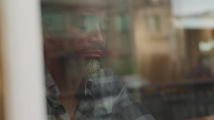 Man closes his eyes sitting in front of wide window reflecting building next door