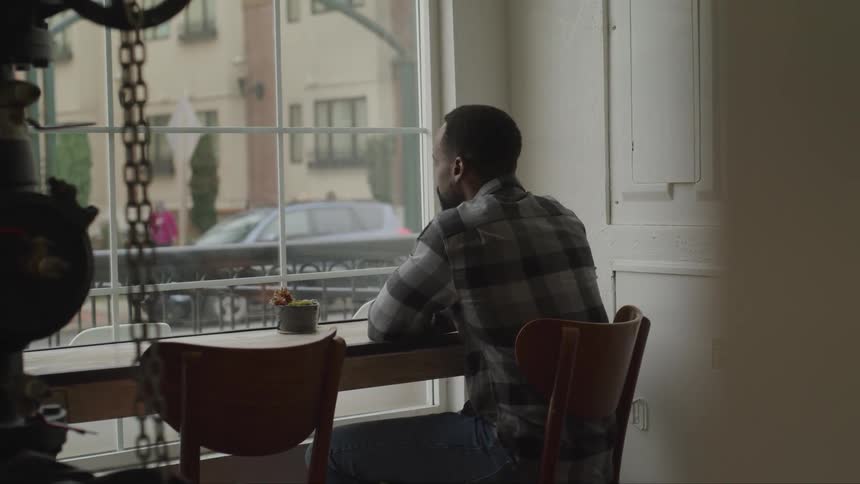 A man sitting in a cafe drinks his coffee as he watches people walk past