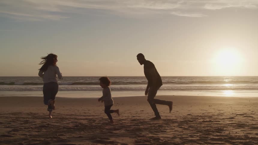 A mother and father running with their daughter on the beach