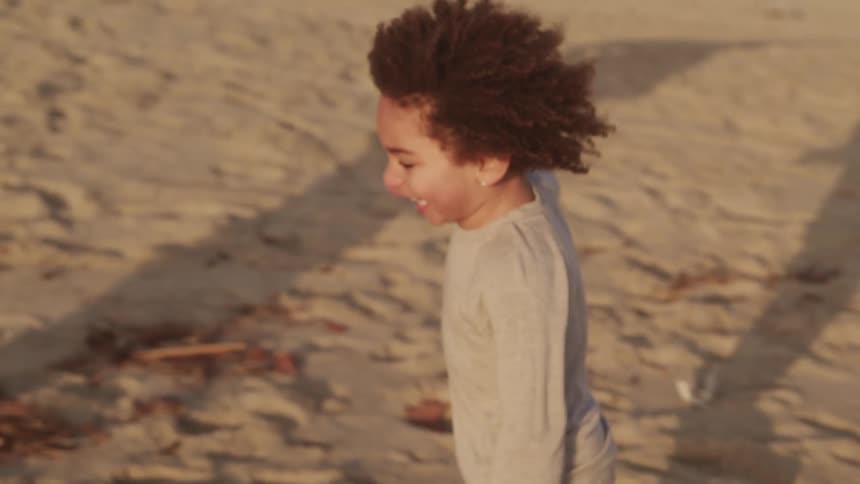 Colored toddler boy runs barefoot on the sand beach at sunset