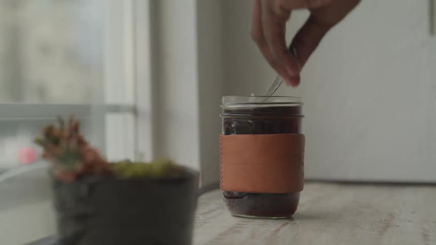 Person stirs steaming beverage sitting near houseplant and window