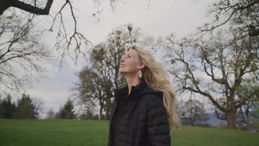 Middle aged blonde woman with a black coat looks up at the sky on a cloudy day