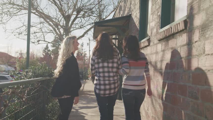A group of friends walks and talk to each other on the pavement next to a building