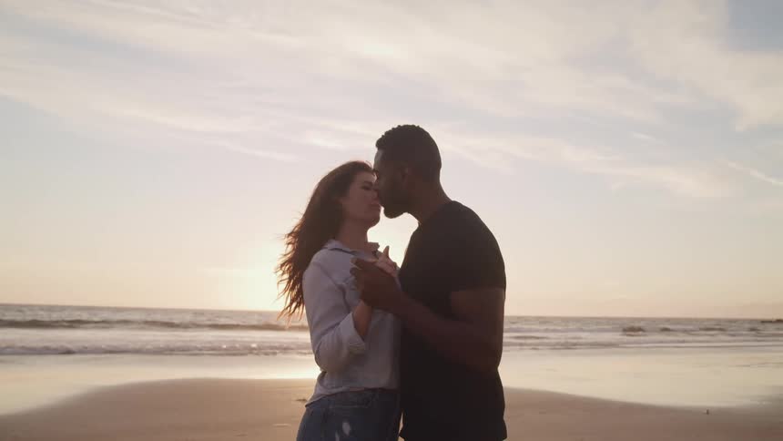 A husband and wife are kissing at the beach