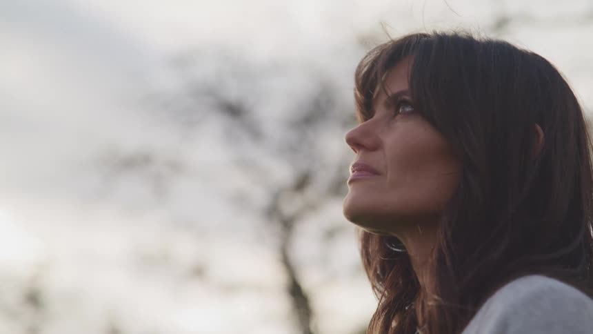 Side view of a brunette woman with dark hair looking up at the sky