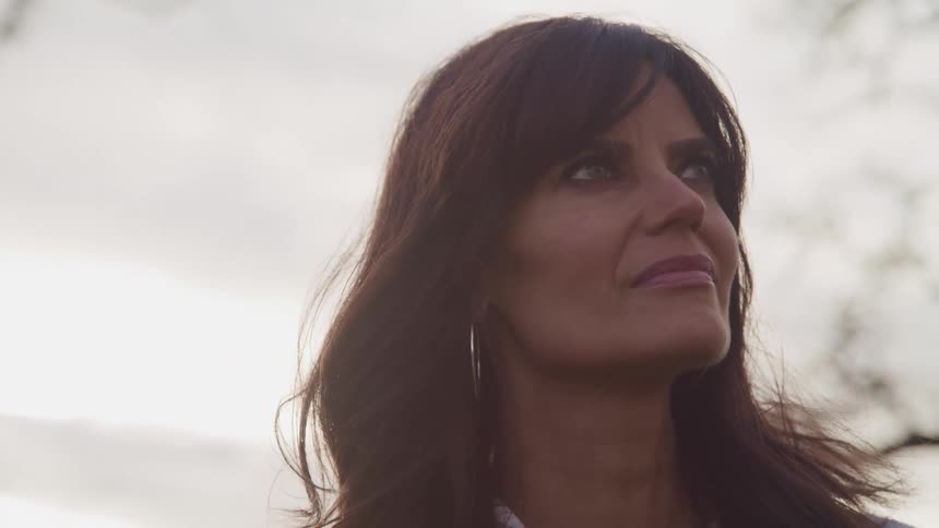 A middle aged woman looks at the sky while standing outdoors during the day