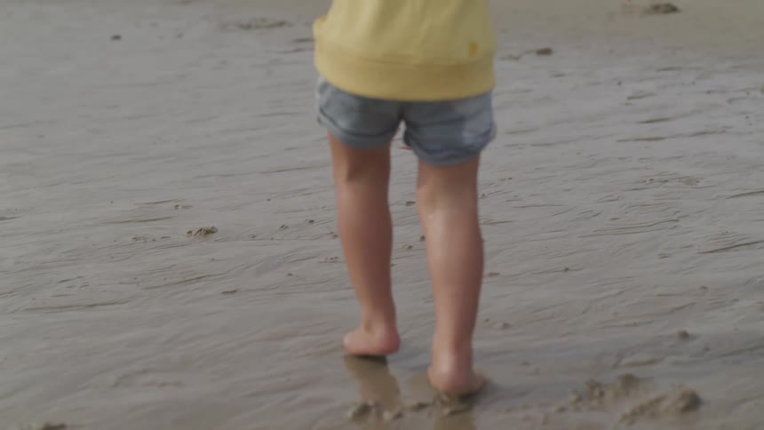 Child wearing shorts runs barefoot across wet sand