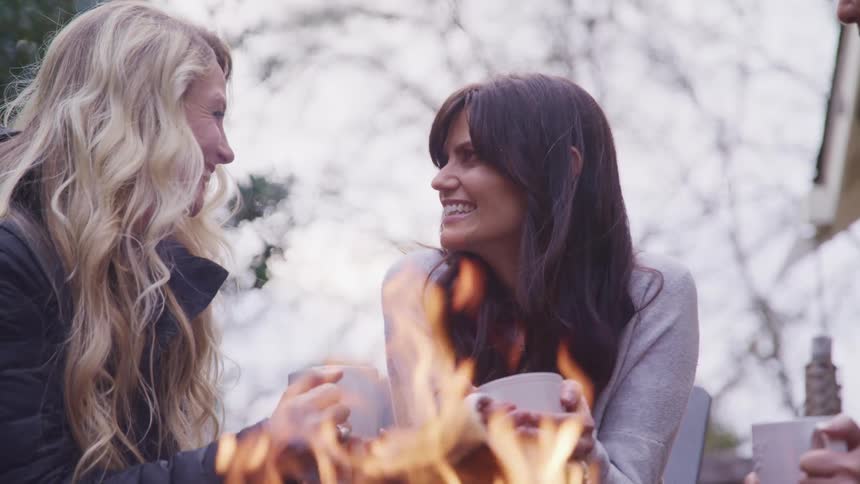 Three women laugh and drink by the campfire