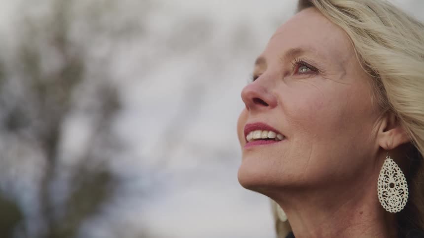 Side view of a blonde woman with makeup and earrings looking up and smiling