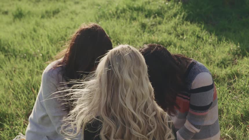Three women sit together in the grass