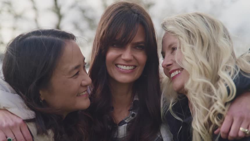 Three women smile and pose in front of a bare tree