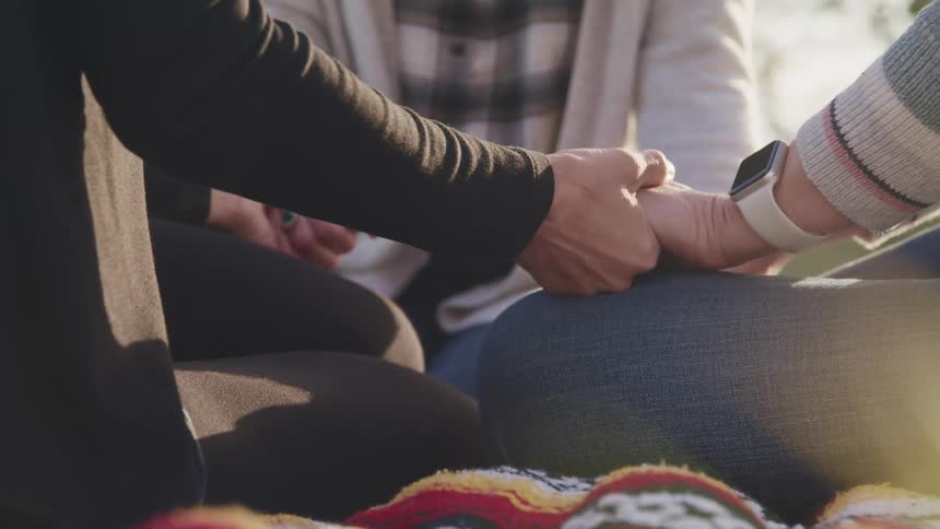 Three friends are sitting outdoors and holding hands