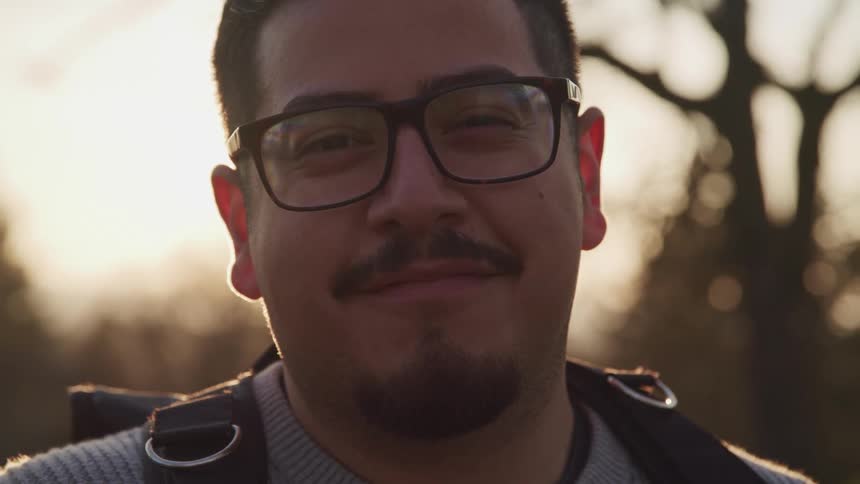 A man is smiling outdoors at dusk