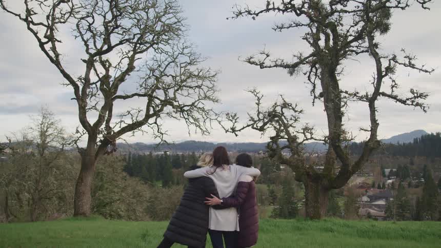 Three women are hugging outdoors