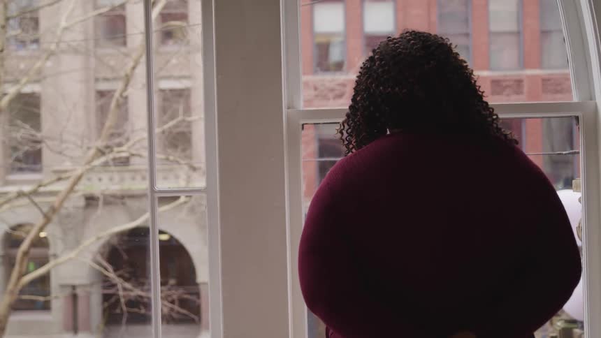 Black chubby woman with a red sweater and curly hair looks out the window