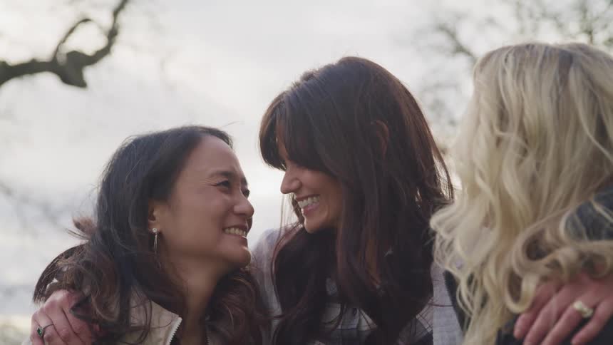Three happy woman hugging and laughing outdoors