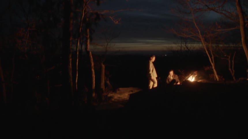 Men stand around a campfire in the woods at night