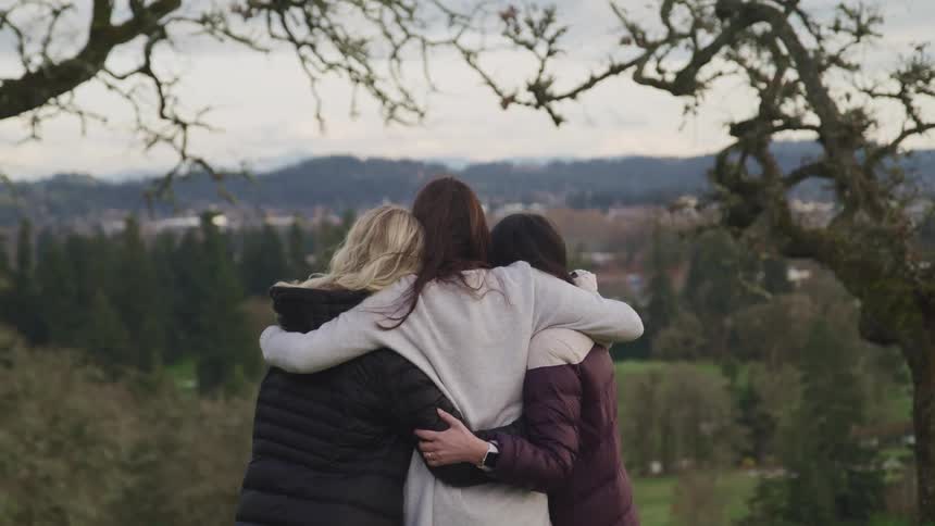 Three women are hugging outdoors