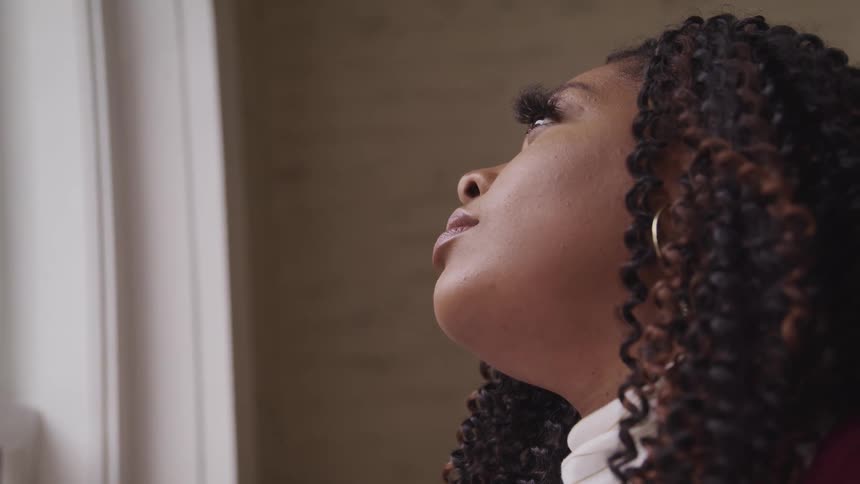Side view of a black woman with makeup and curly hair looking out the window