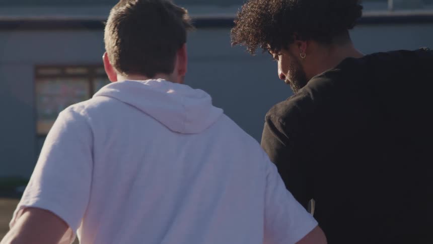 Two male friends playing basketball outdoors at sunset