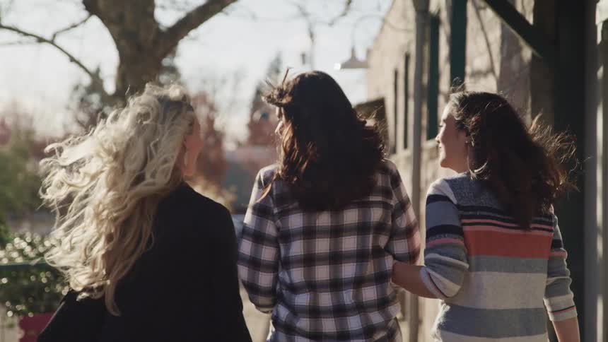 Three women walk down the block arm in arm