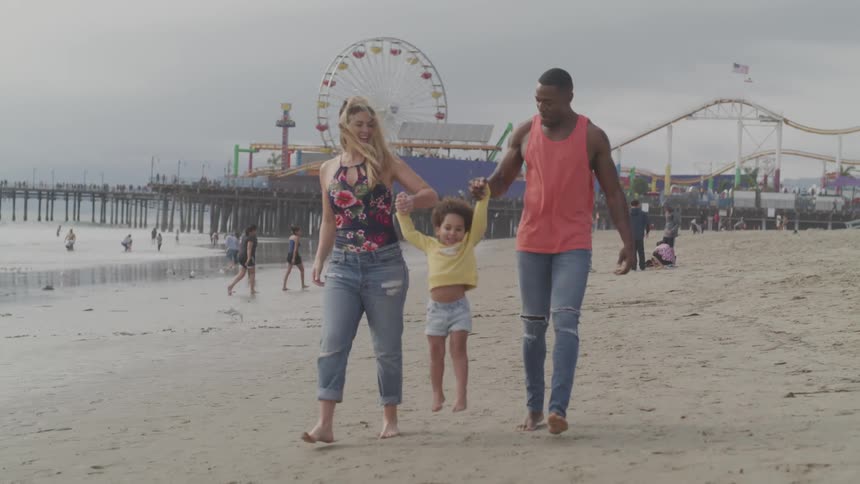 A man and woman swing a little girl between them as they walk along a beach
