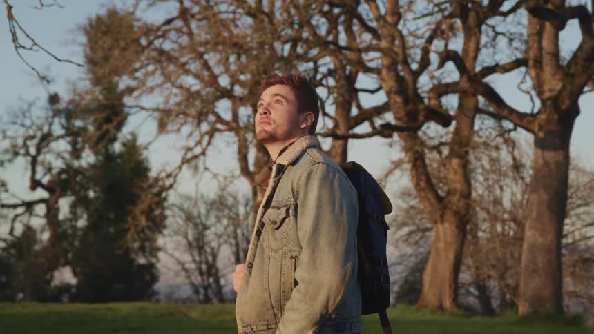 A teen walking across the grass turns and looks up and behind him