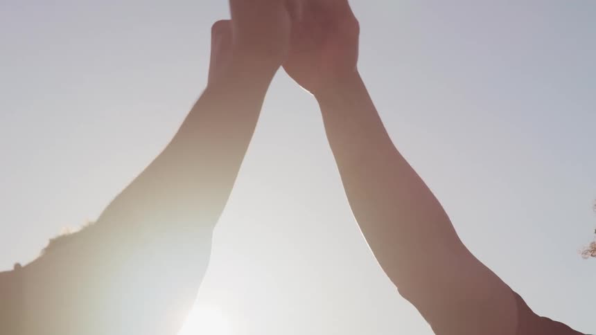 Three male friends raise their arms and fist bump while standing outside