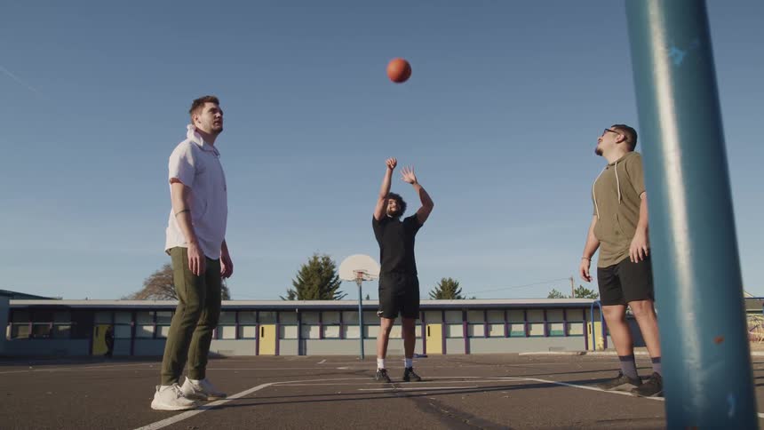A man takes a free throw shot with a basketball as his two friends get ready to get the rebound
