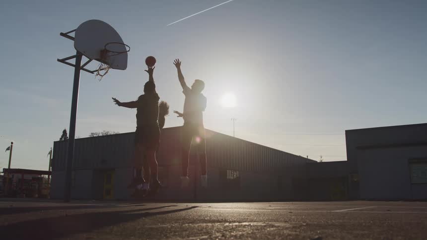 Three men playing basketball with buildings the sky and clouds in the background