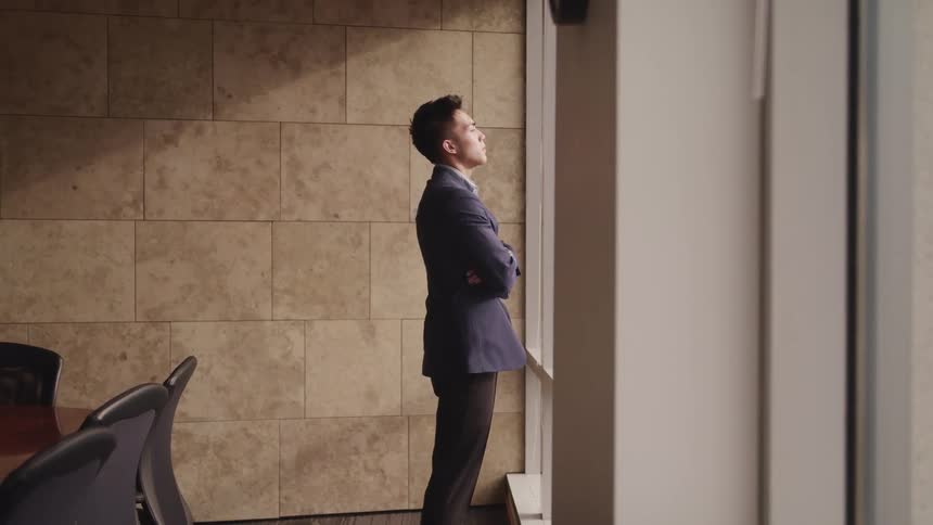 Asian businessman in a suit looks out the windows in the office