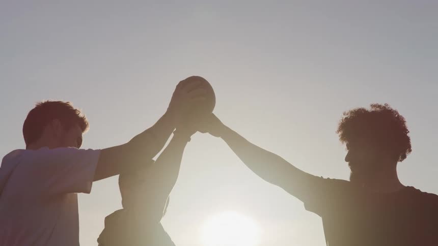 Silhouette of a group of friends fist bumping on a football at sunset