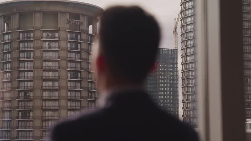 Businessman wearing a black suit looks out office windows in the office