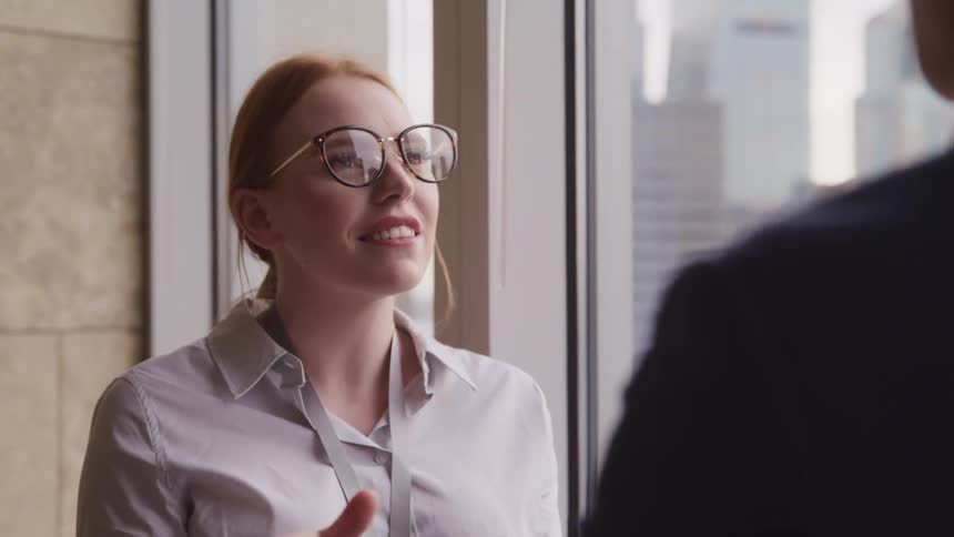 Businesswoman with glasses and red hair talks to businessman wearing a suit in the office