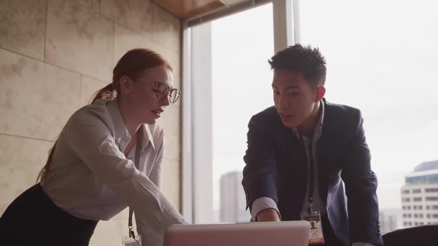 Business woman red hair glasses and asian man with a suit look at a laptop in the office