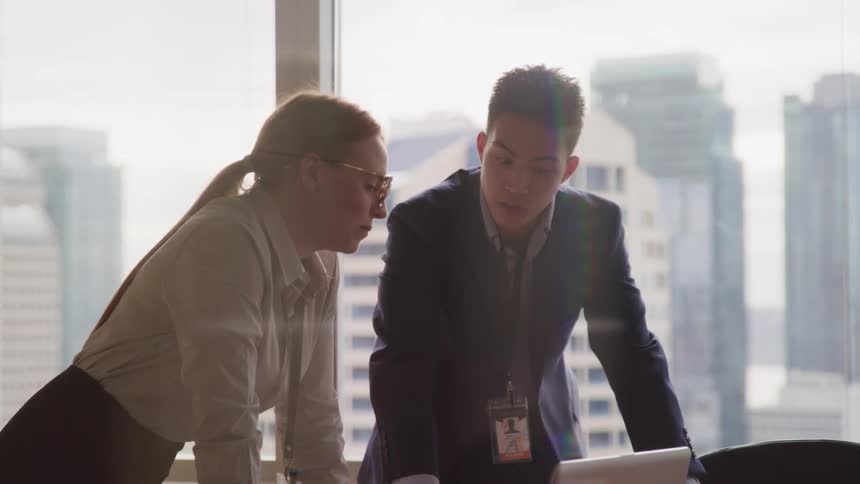 Man and woman lean on a desk as they talk in an office