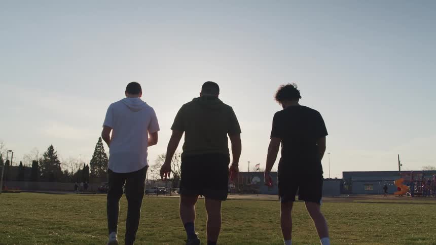 Men walk across field toward playground with football talking