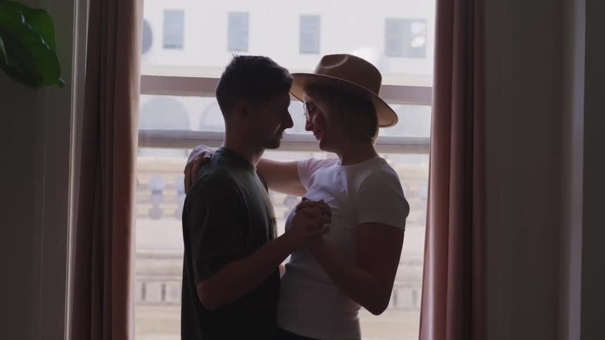 Man with a t shirt and blonde woman with glasses and a hat dancing together are silhouetted
