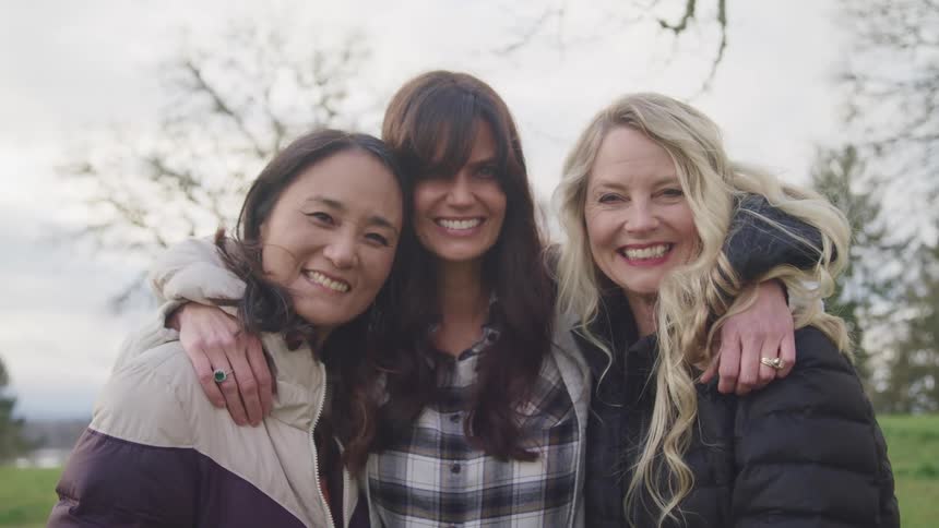 Group of women hug and smile while looking at the camera in a field