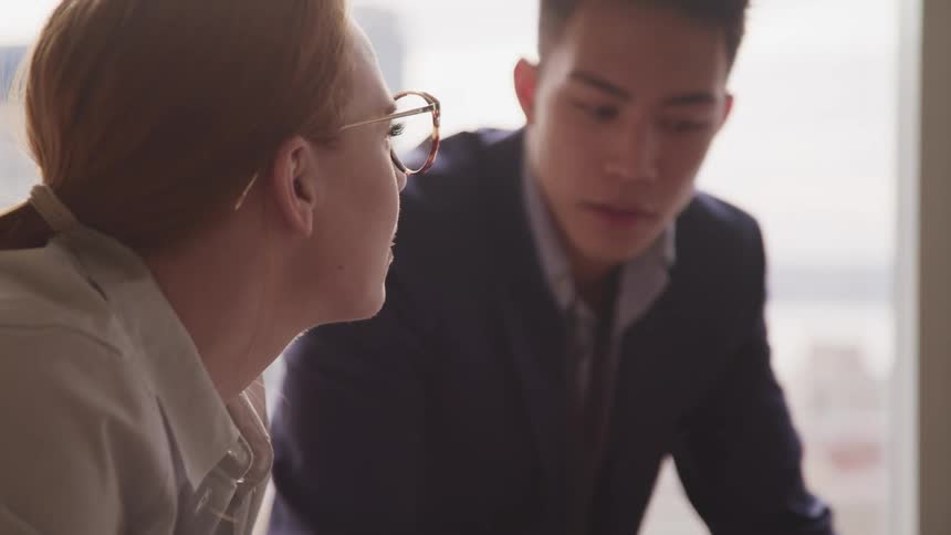 People in formal business attire sit near window consulting