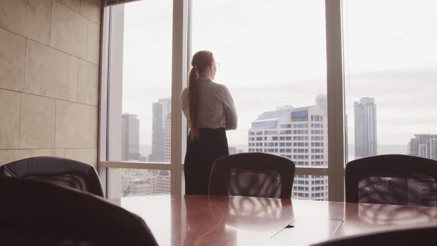 A woman is standing in a conference room and looking out a window