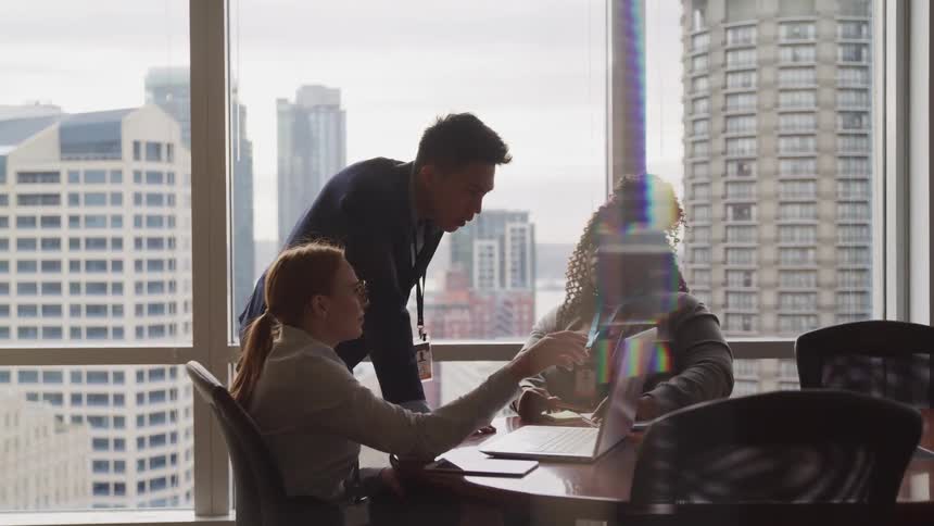 Three people converse around a meeting desk in a high rise office