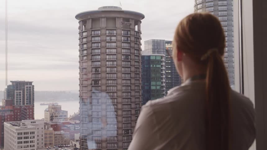 A woman is looking at the buildings from the window