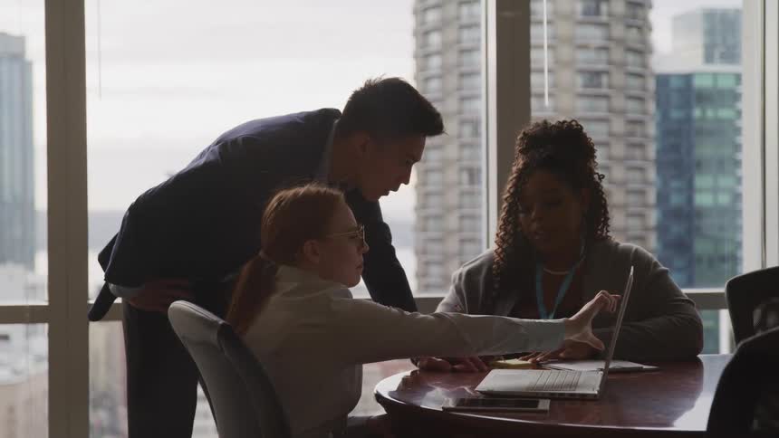 Workers in an office talk together by a laptop