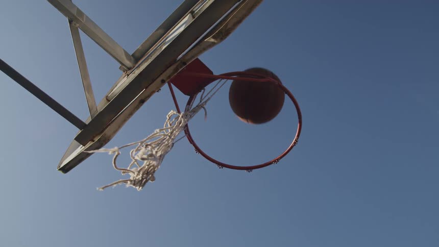 A basketball falls through a basketball hoop with a dangling net