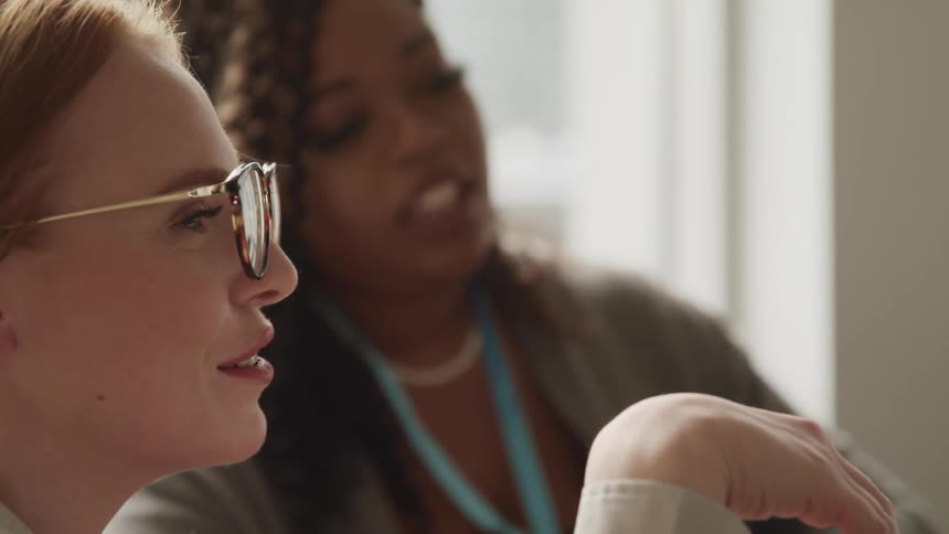 Two women looking at something outside the frame talk to each other in a room