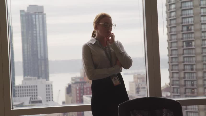 A woman standing in a conference room with a window and buildings in the background